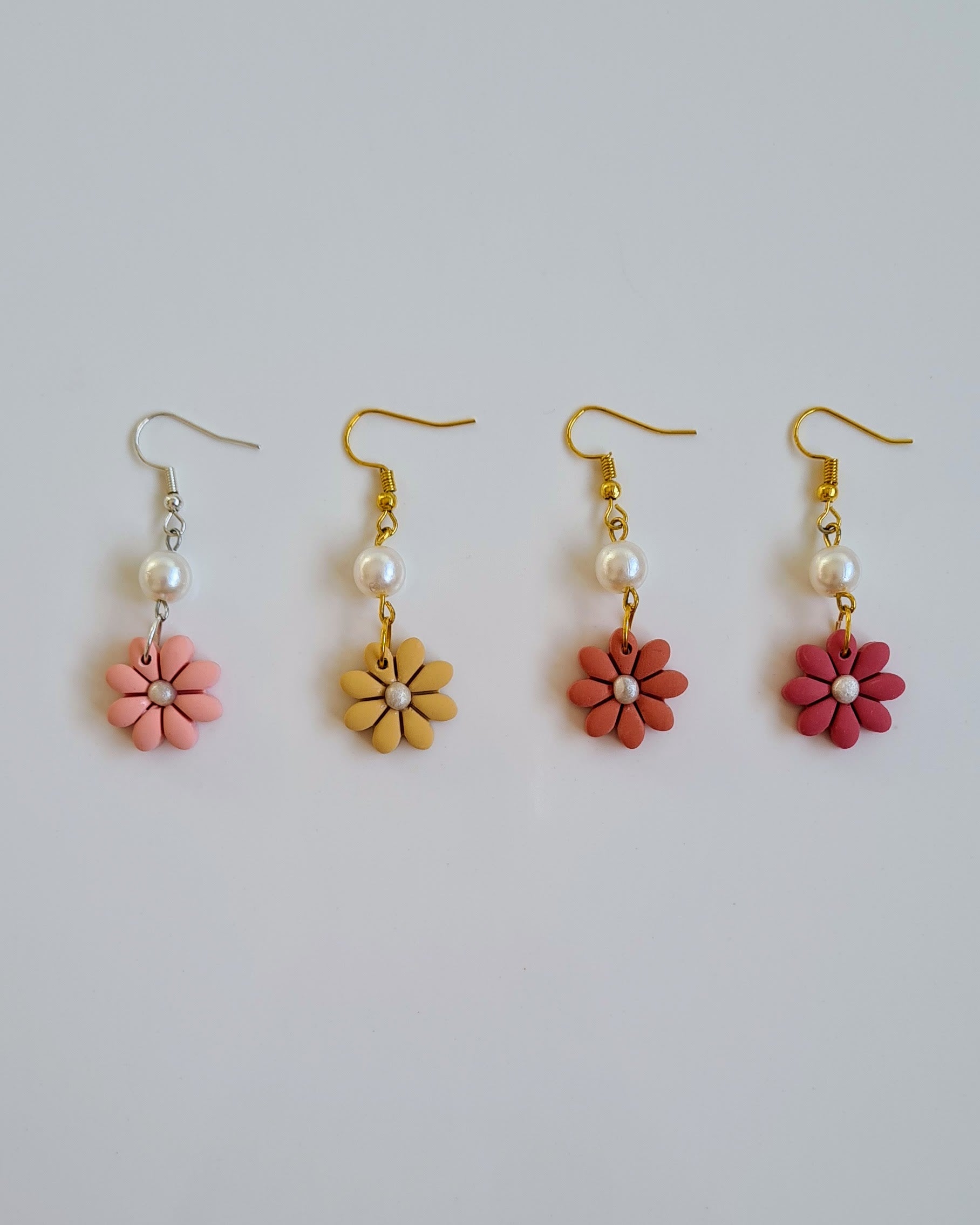 Set of four flower-shaped earrings with pink, yellow, orange and red flowers on a light grey background.