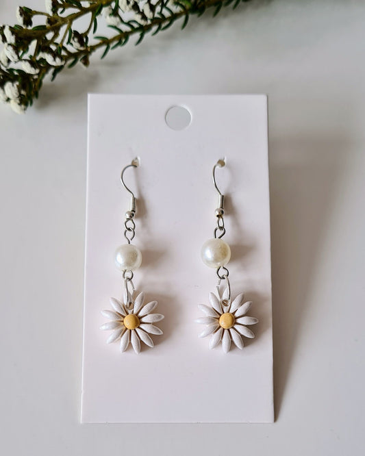 Pair of daisy-shaped earrings on a white card with greenery around.