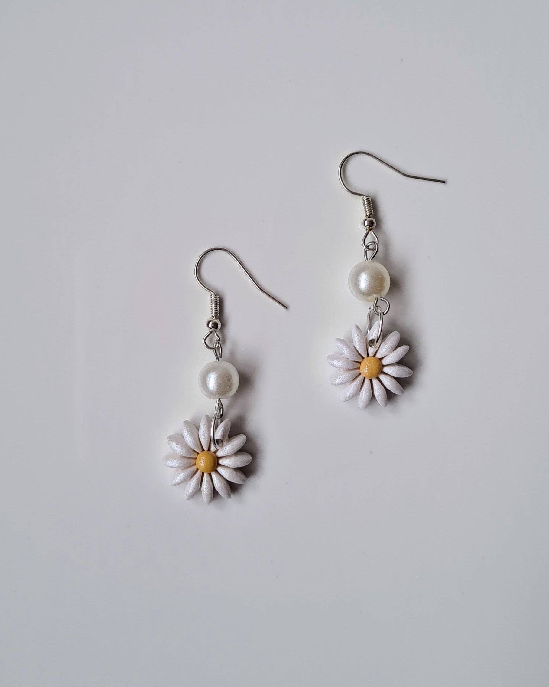 Pair of daisy flower earrings with pearl accents on a light gray background