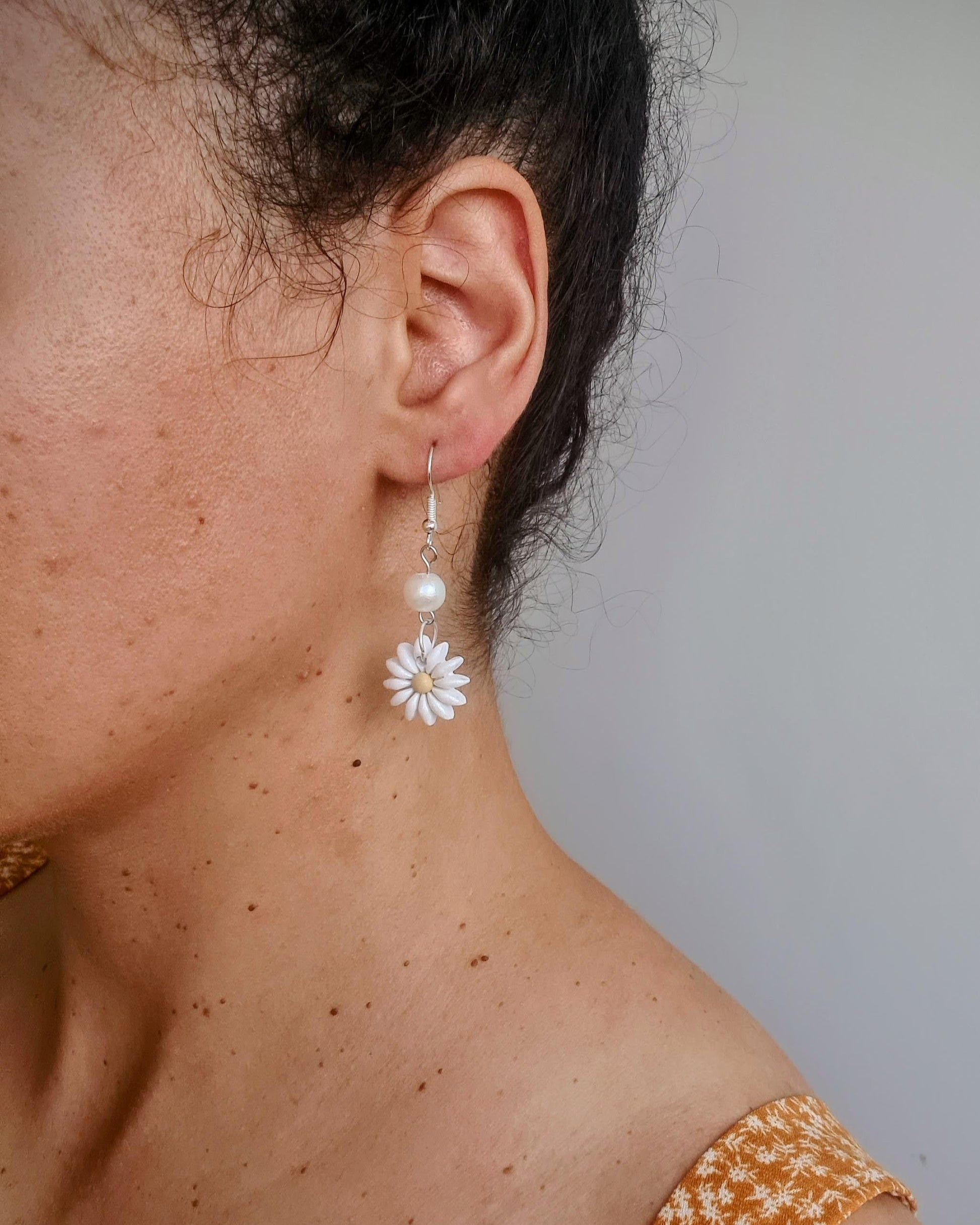 Close-up of a person wearing a floral earring with a plain background