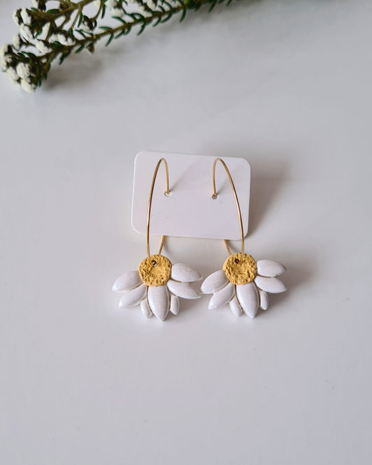 White daisy hoop earrings with yellow centers on a white background with greenery.