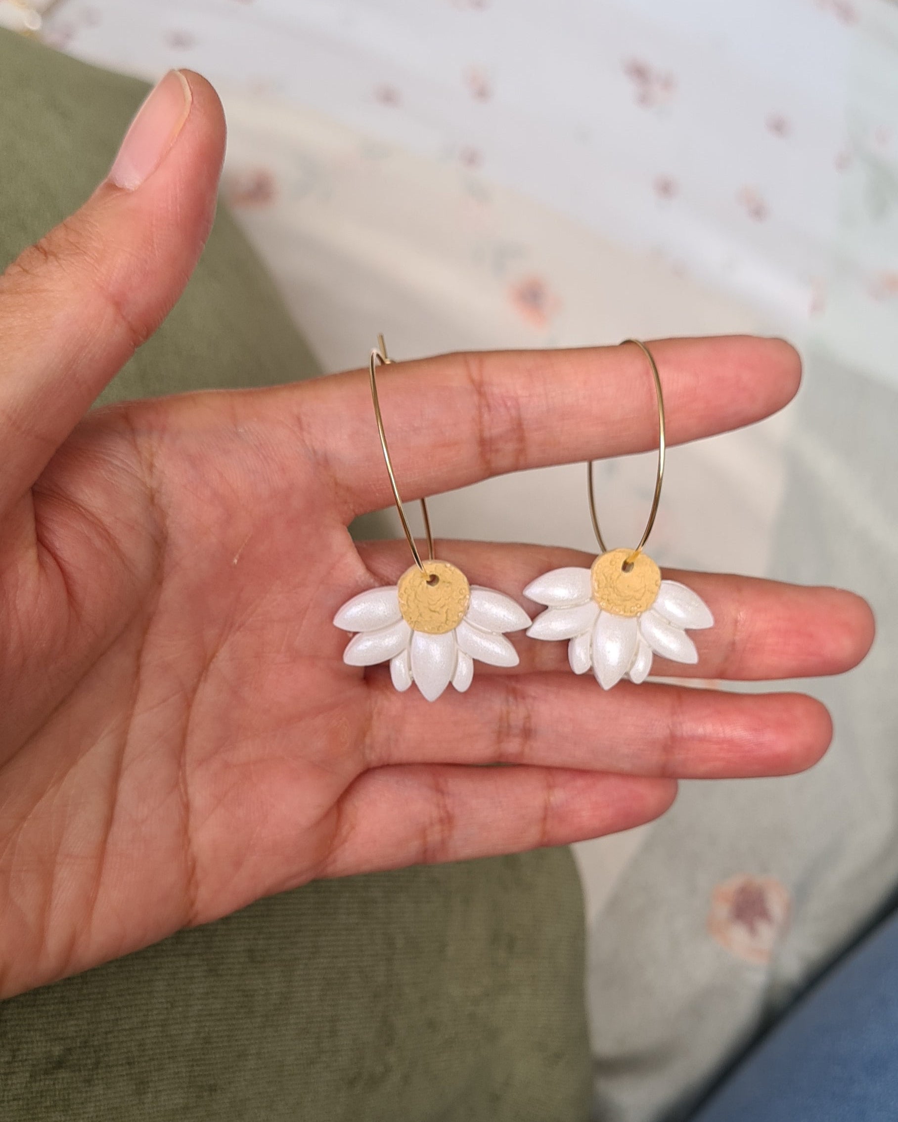 Hand holding two small flower-shaped daisy hoop earrings with a blurred background