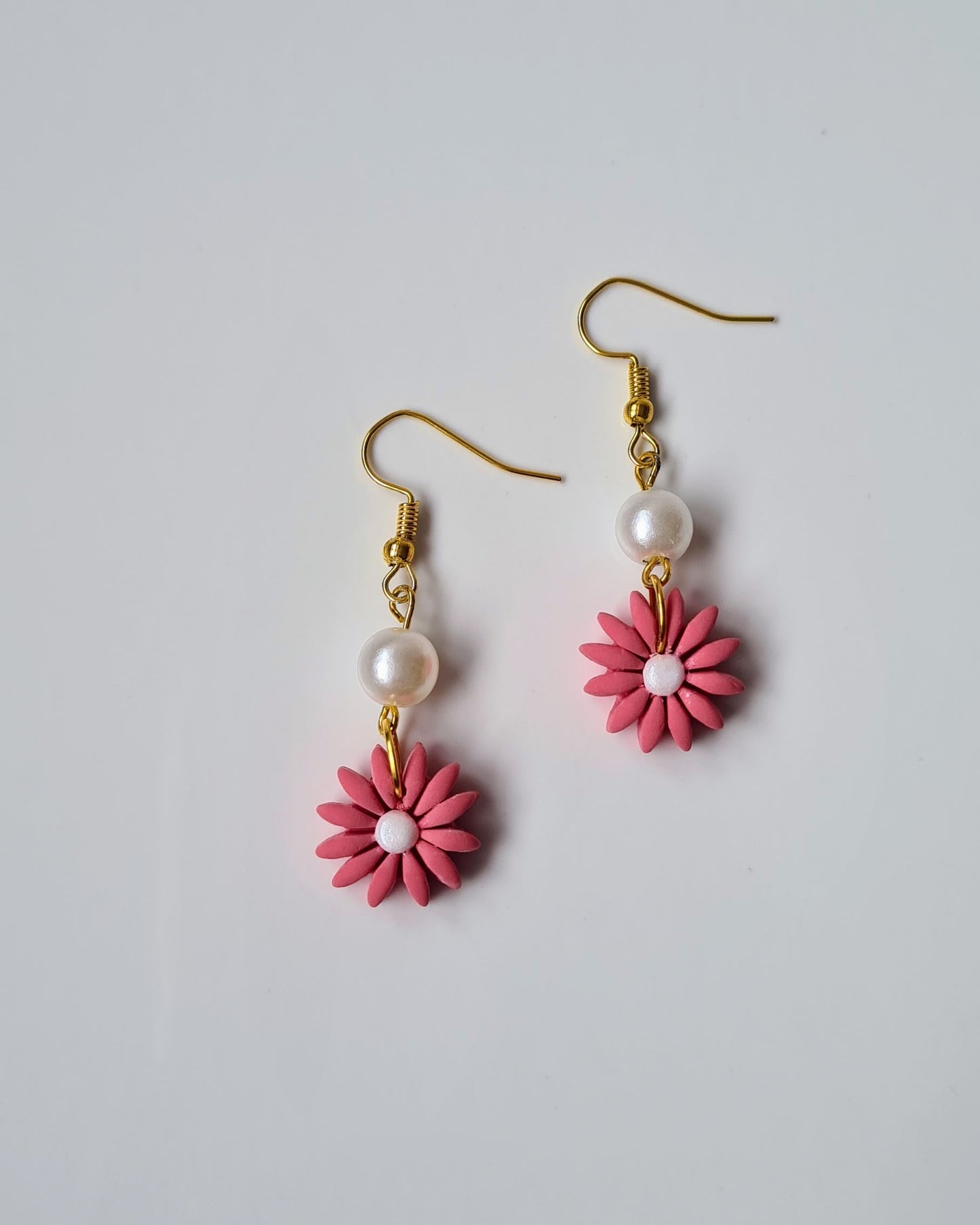 Pair of pink flower-shaped earrings with gold hooks on a light gray background