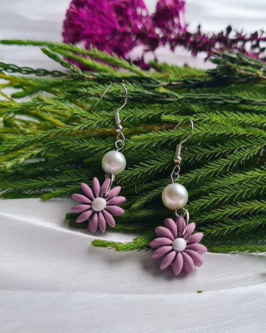Lavender flower earrings with pearls on a white surface with greenery