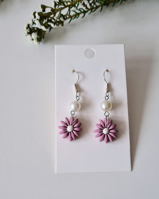 Pair of Lavender flower-shaped earrings on a white card with greenery around.