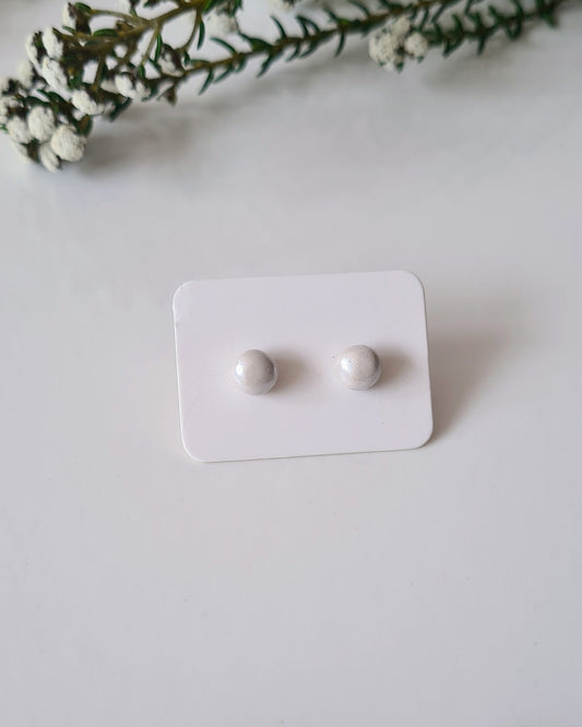Pair of white earrings on a white card with greenery around