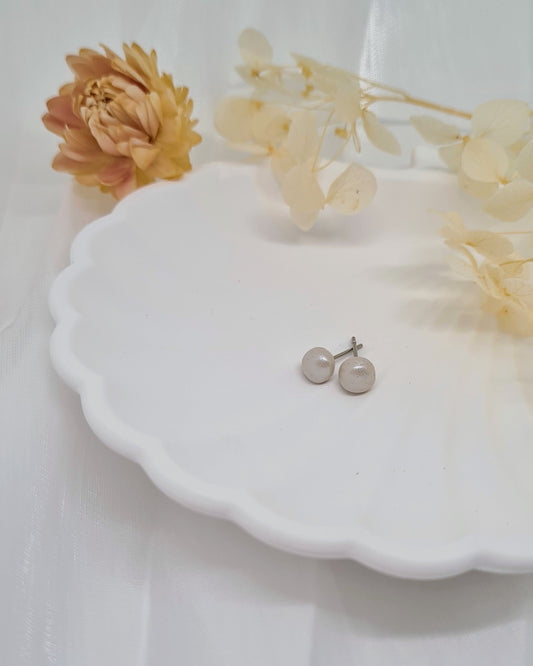 Pair of earrings on a white dish with flowers against a light background