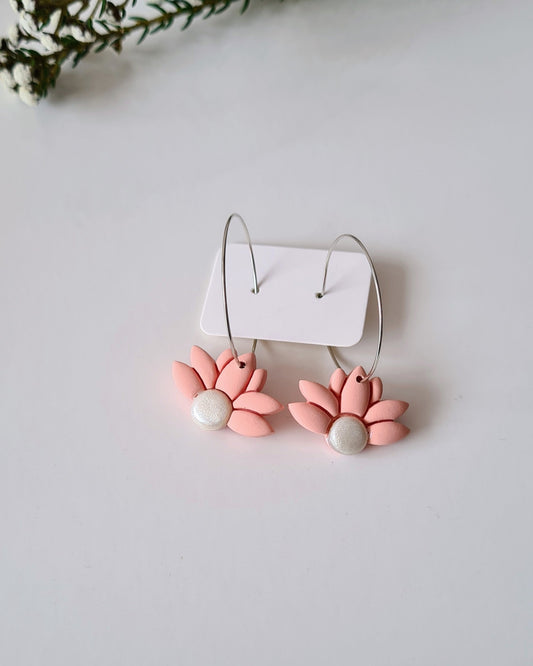 Pair of floral hoop earrings with a white holder on a white background with greenery.