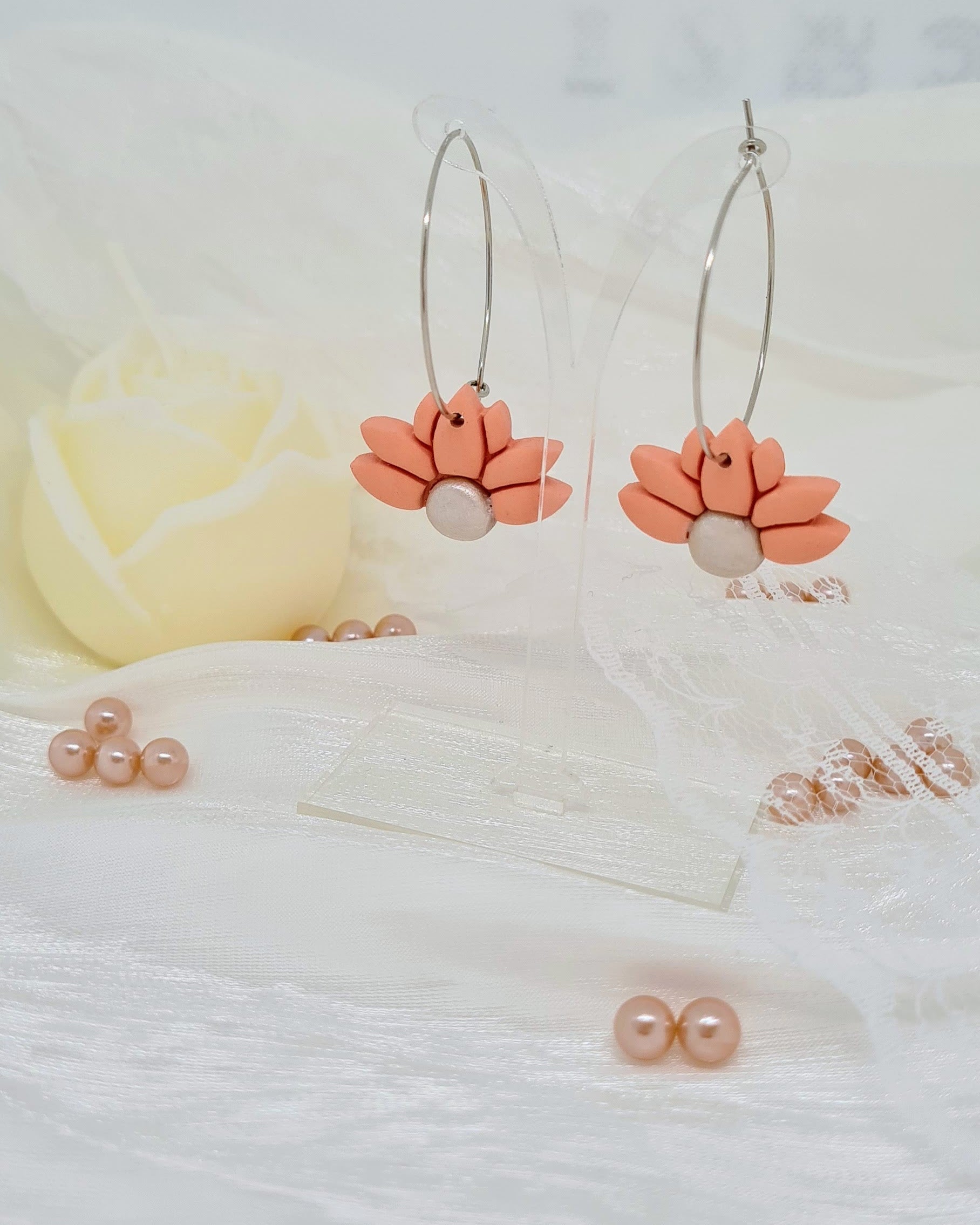 Floral hoop earrings on transparent stand on a satin white surface with a blurred background