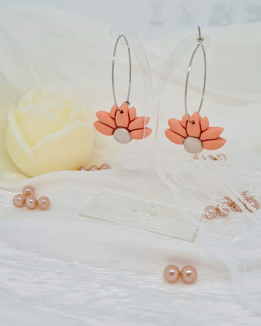 Floral hoop earrings on transparent stand on a satin white surface with a blurred background