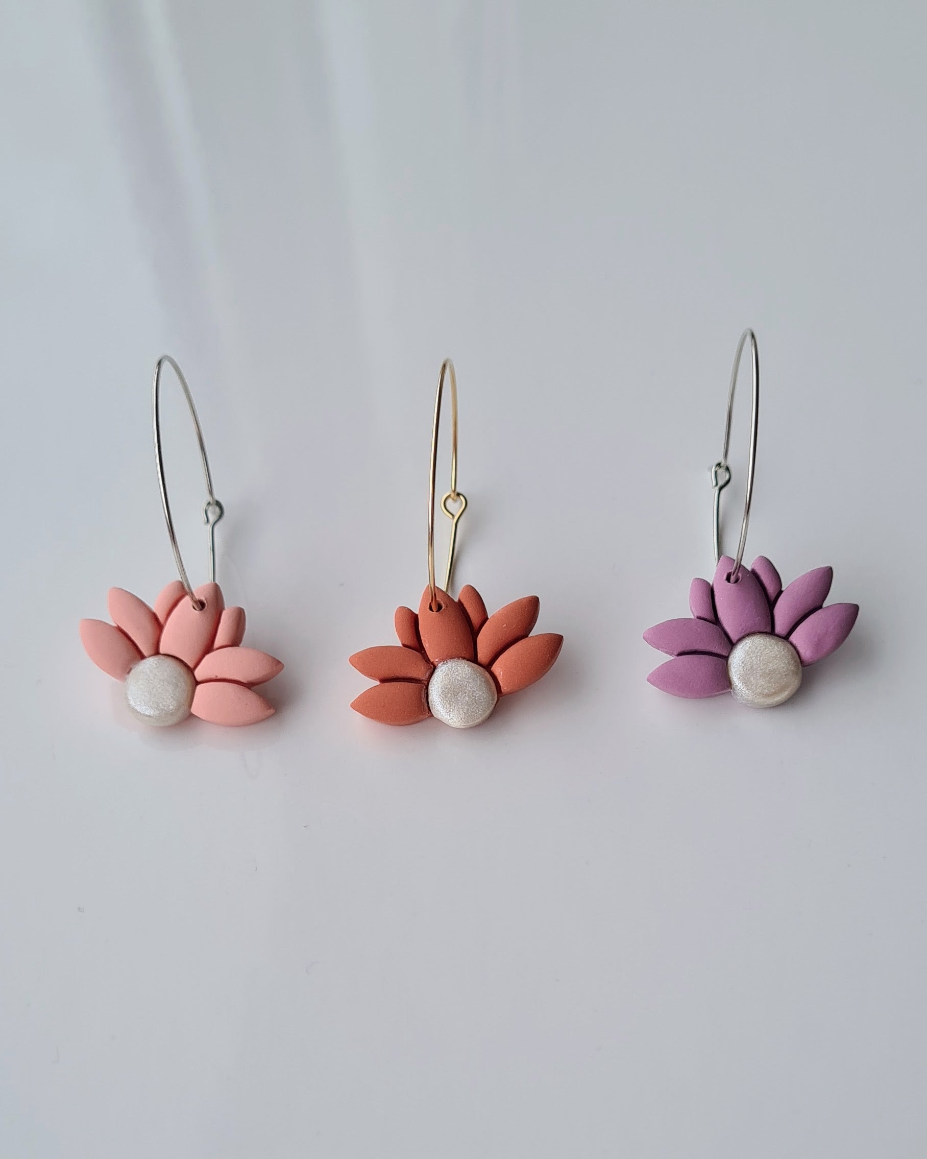Three lower-shaped hoop earrings on a light grey background