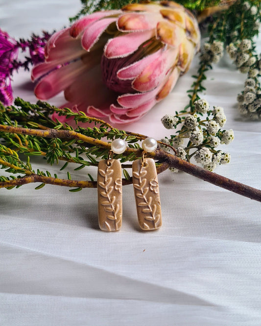 Shimmery yellow earrings with floral design and pearl accent on a white surface with flowers.