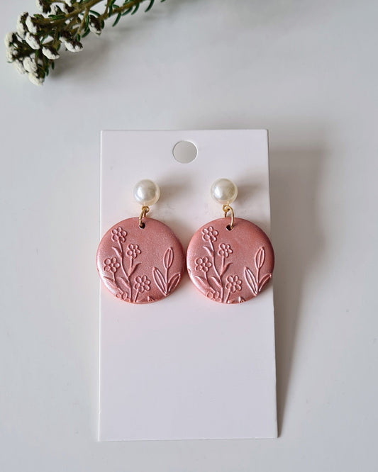Orange earrings on a white card with greenery around