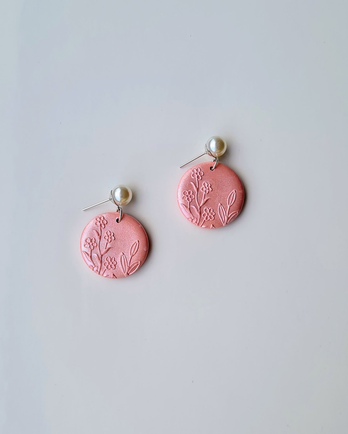 Pink earrings with floral designs on a light gray background