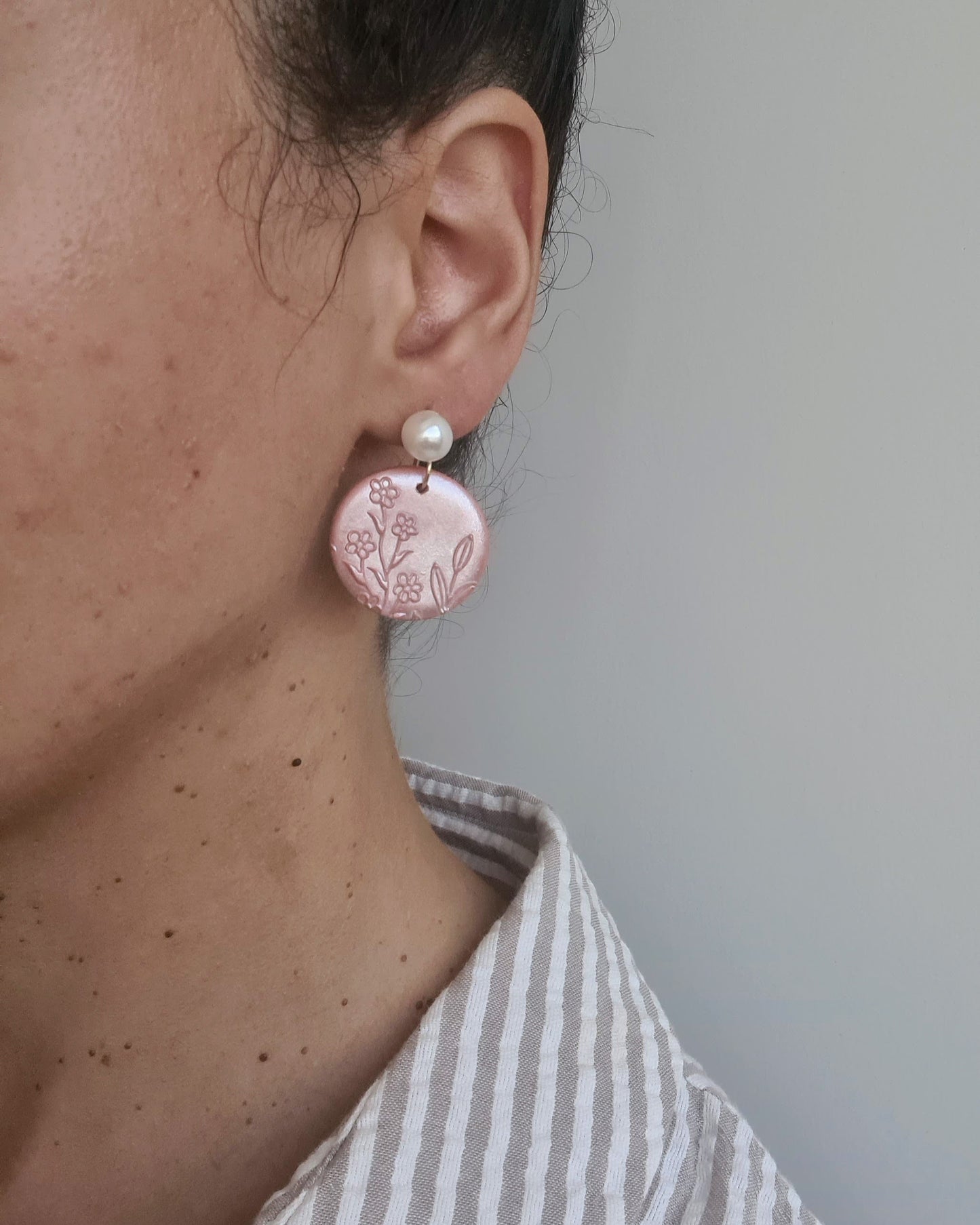 Close-up of a person wearing orange shimmery earrings with floral patterns against a neutral background