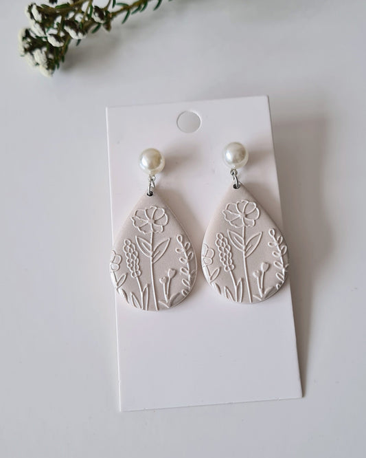 White leaf-patterned earrings on a white card with greenery around