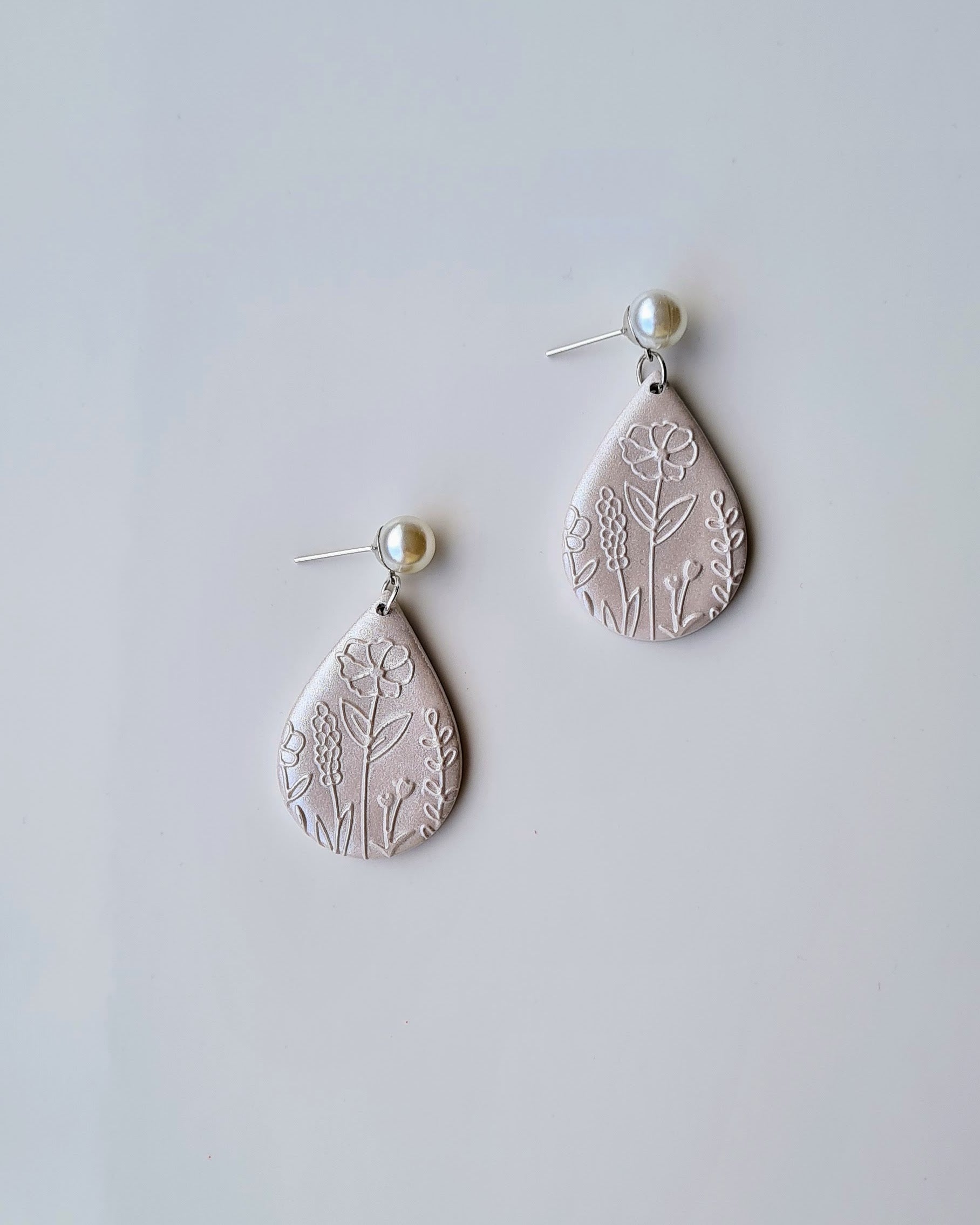 Teardrop-shaped earrings with floral patterns and a shimmery finish on a light grey background