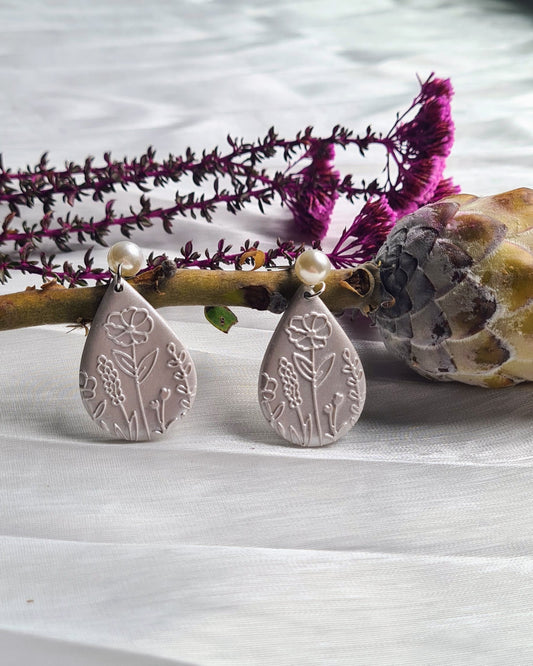 Teardrop-shaped earrings on a white surface with a branch and flowers in the background