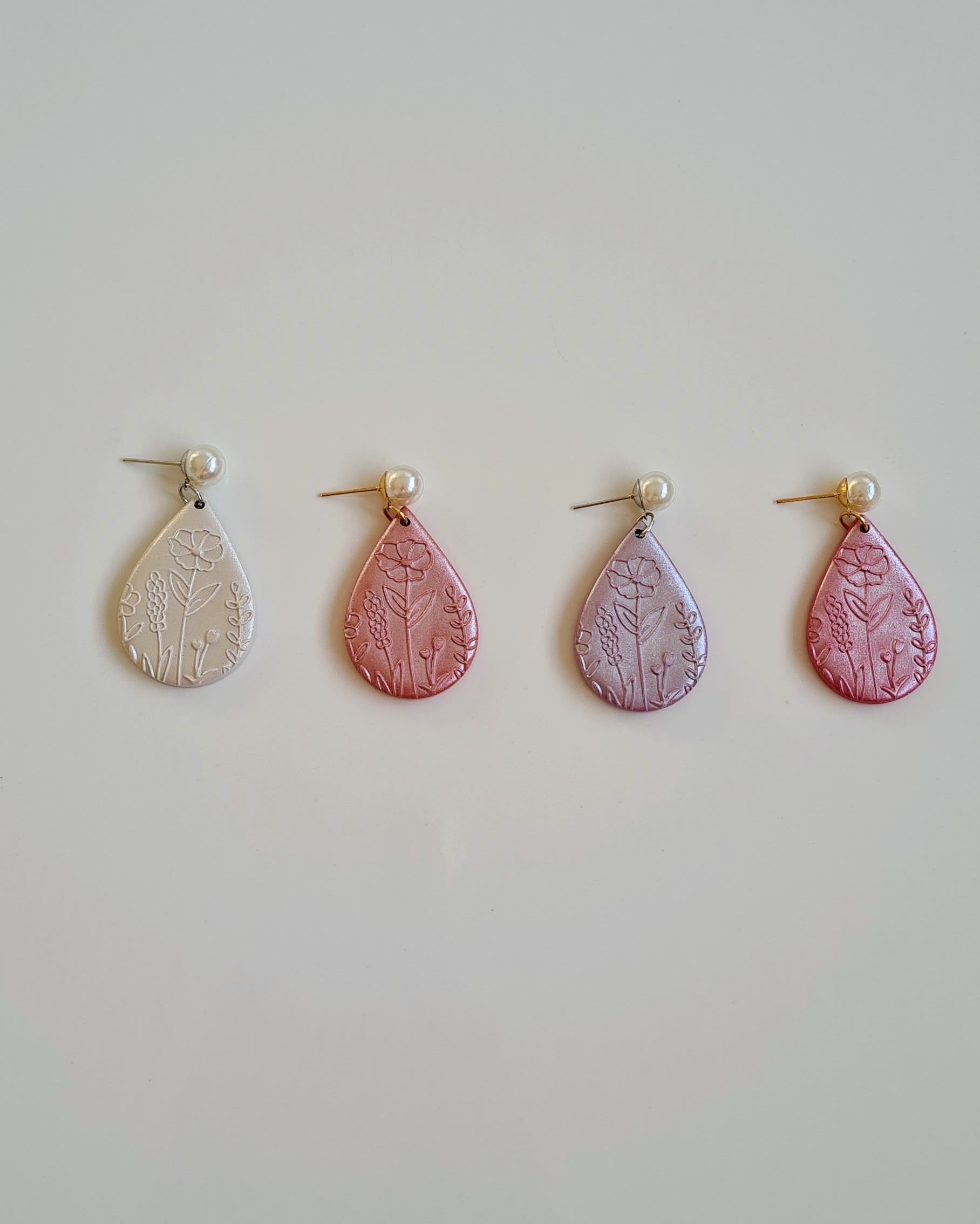 Four pairs of drop earrings with floral patterns on a light grey background