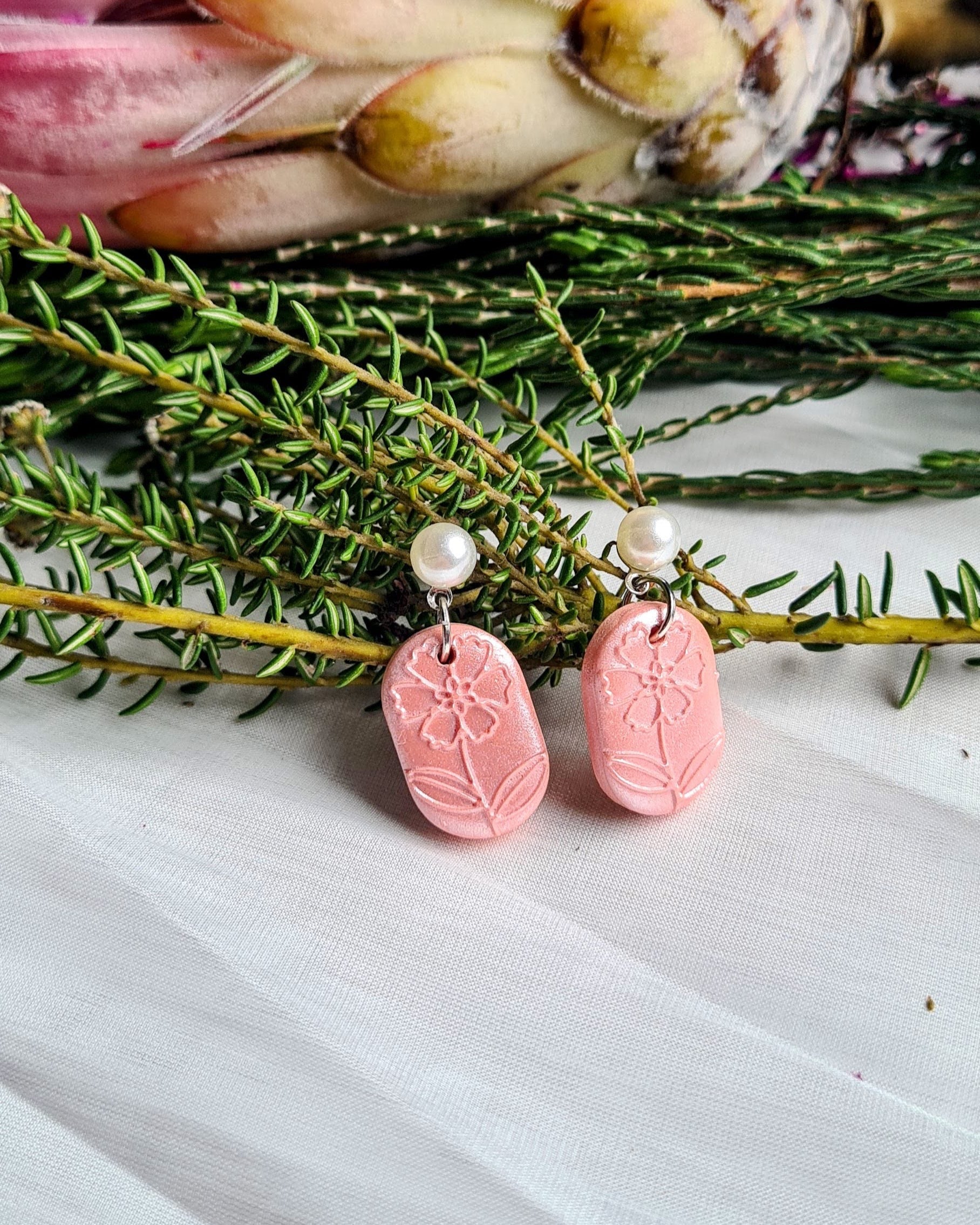 Pink earrings with a pearl accent on a satin surface with greenery