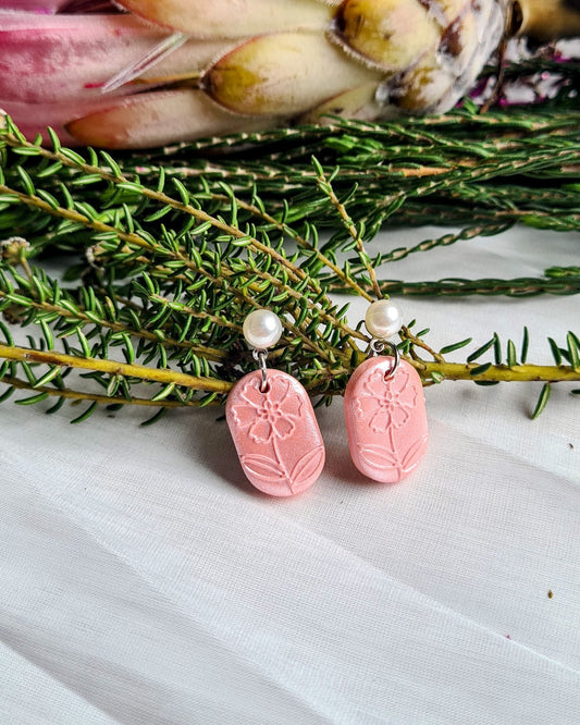 Pink earrings with a pearl accent on a satin surface with greenery