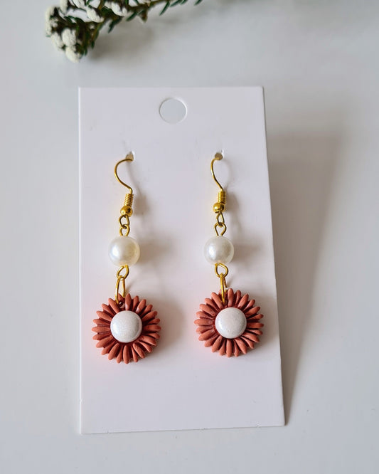 Pair of drop earrings on a white card with greenery around