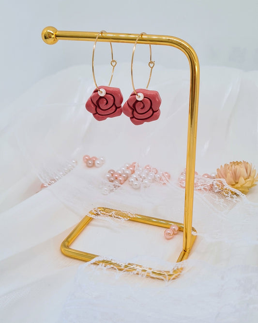 Rose-shaped earrings on a gold stand with a floral background