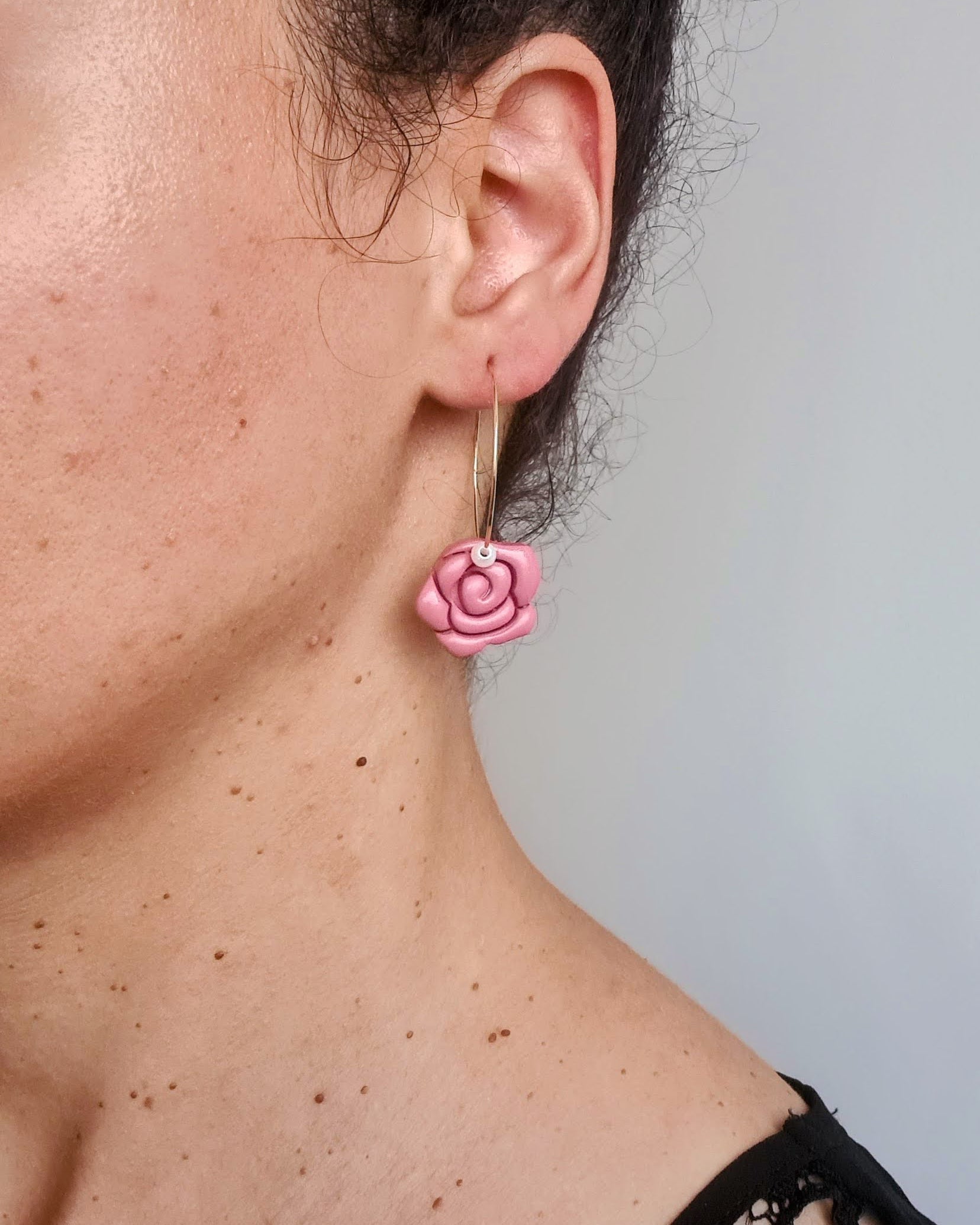 Close-up of a person wearing a red rose-shaped earring against a neutral background