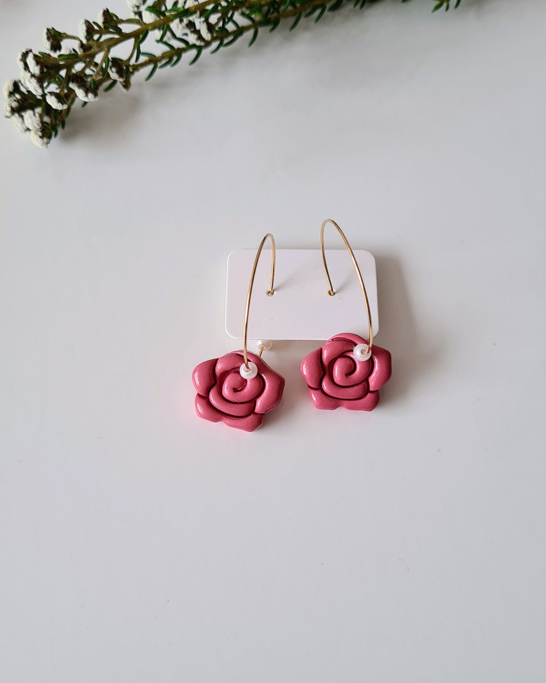 Rose and pearl hoop earrings on a grey background with green branches.