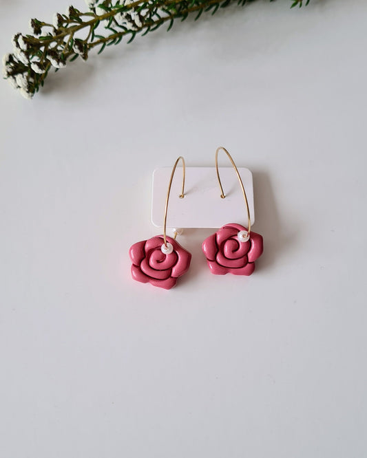 Rose and pearl hoop earrings on a grey background with green branches.