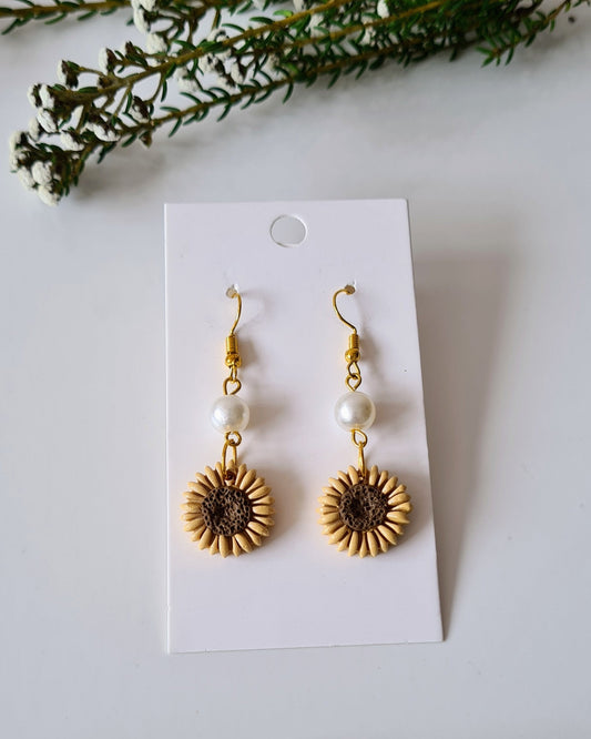 Gold sunflower earrings with pearls on a white card, surrounded by greenery.