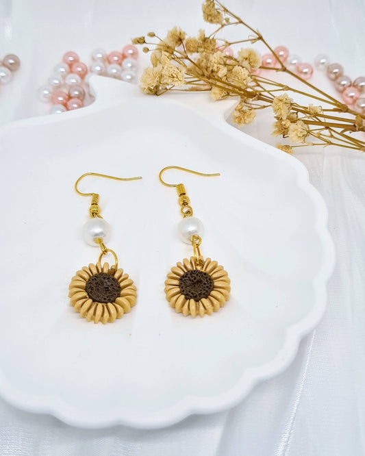 Gold sunflower earrings on a white shell with dried flowers in the background