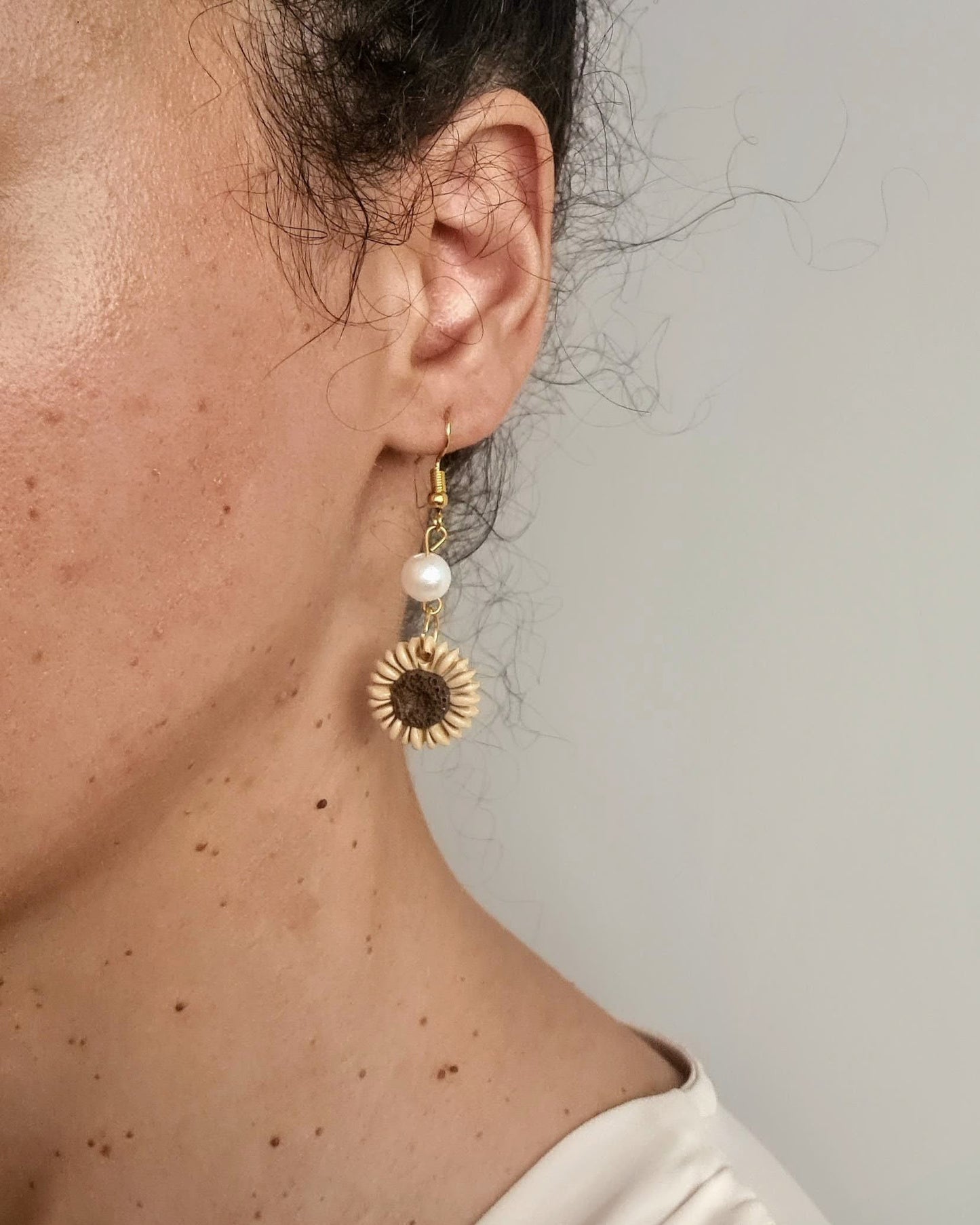 Close-up of a person wearing a sunflower-shaped earring with a pearl center.