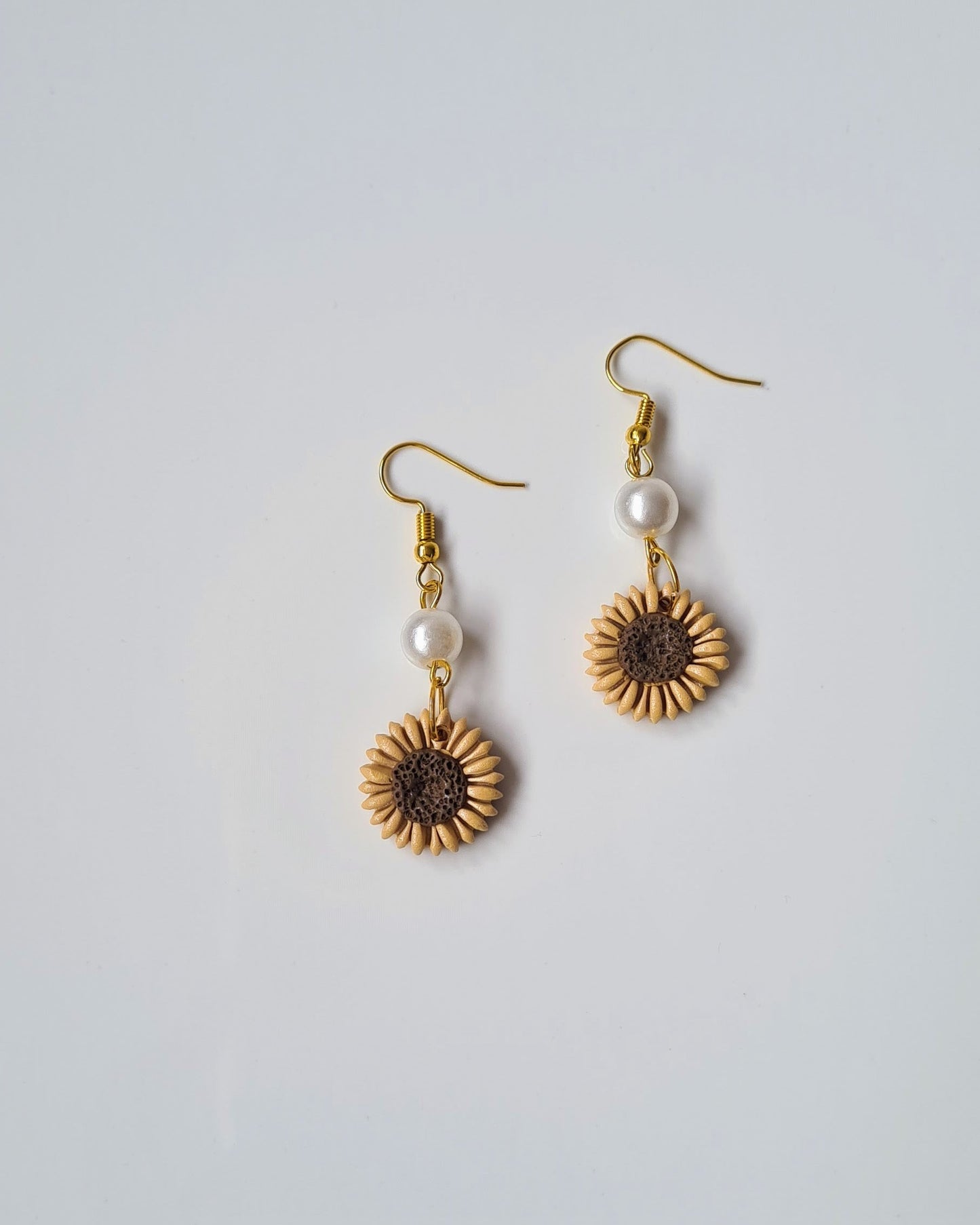 Pair of sunflower-shaped earrings with pearl accents on a light gray background
