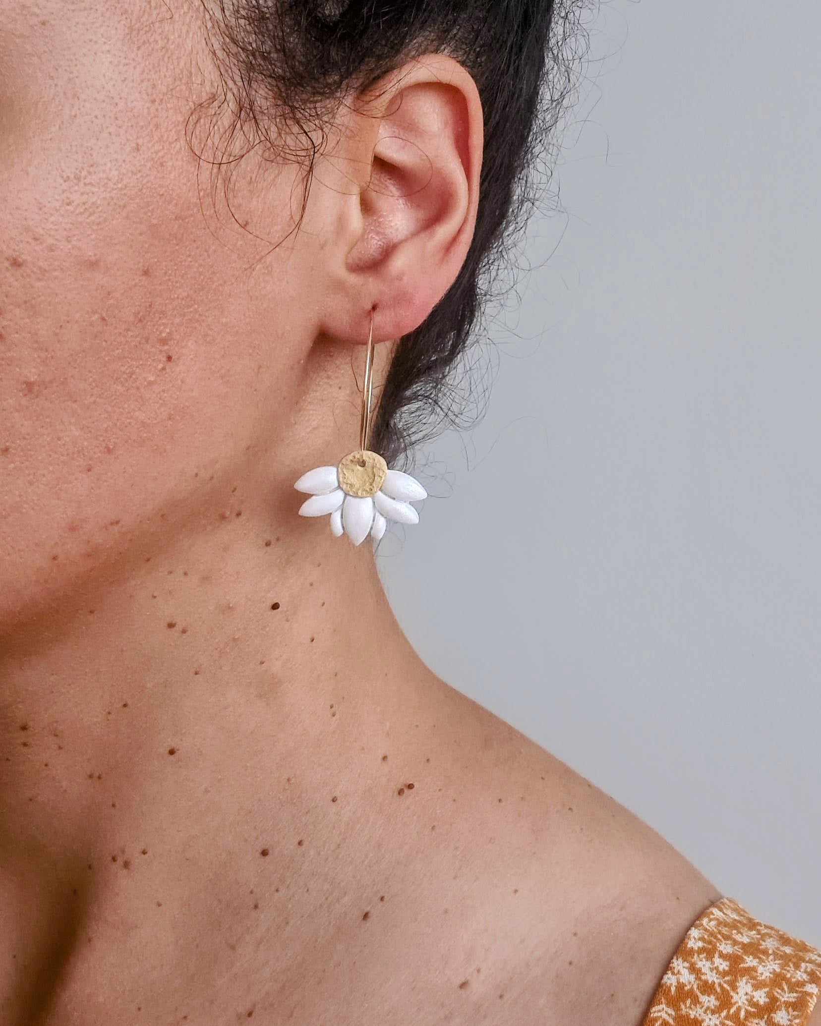 Close-up of a person wearing a daisy flower earring against a neutral background